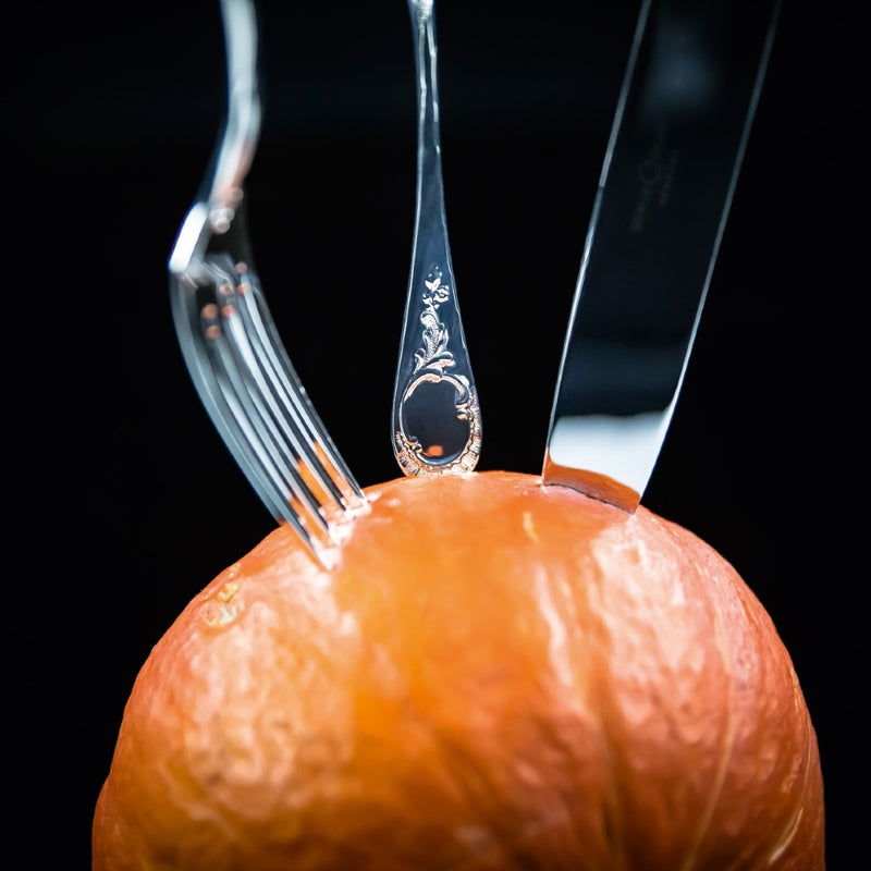 Ornate Vendôme dinner knife with decorative handle cutting orange.