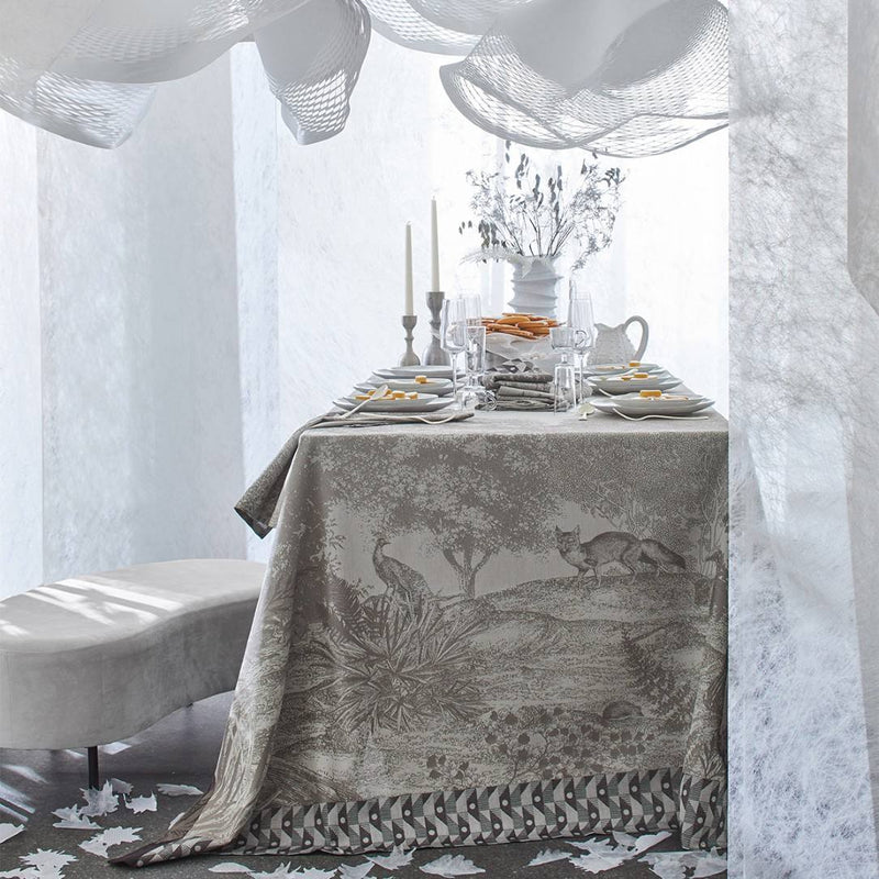 Grey cotton placemat with forest motifs and geometric border on grey luxury tablescape.