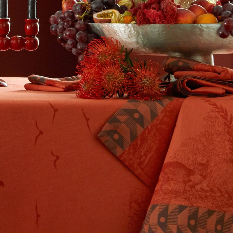 Orange cotton placemat with forest motifs and geometric border styled on luxury tablescape.