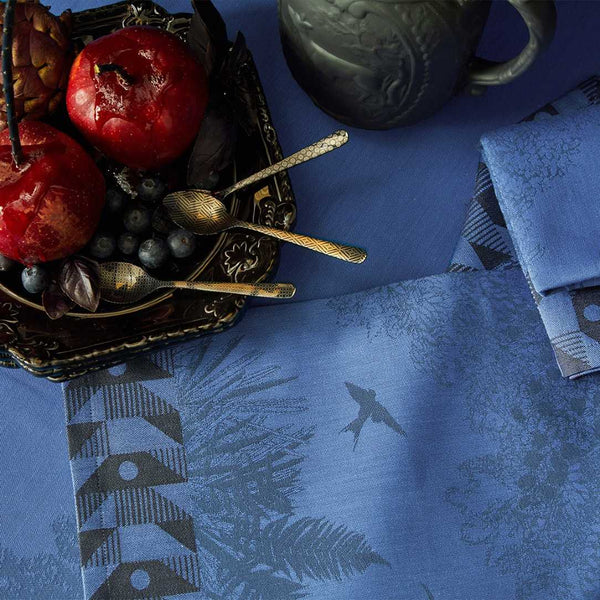 Blue cotton placemat with forest motifs and geometric border close-up.