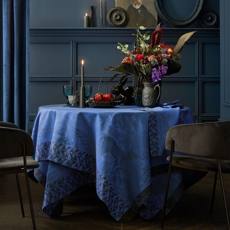 Blue cotton placemat with forest motifs and geometric border styled on luxury tablescape. 