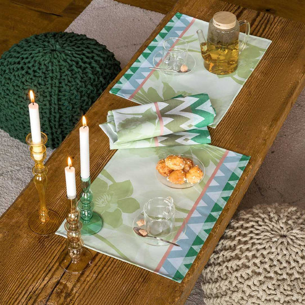 Green coated cotton placemat with jacquard daffodil and chevron design styled on coffee table.