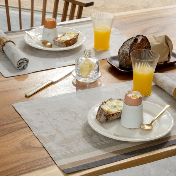 Beige linen placemat with jacquard floral motifs in beige tones on breakfast table setting.