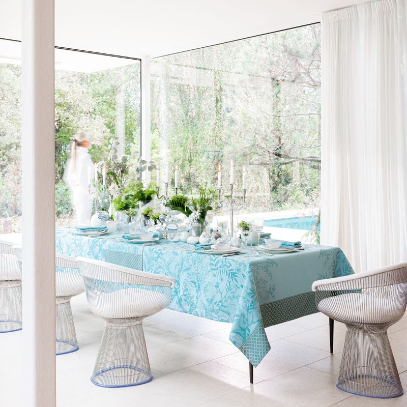 Blue Jardin d’Eden cotton napkin with delicate floral pattern styled on table setting with table linens from the same collection.