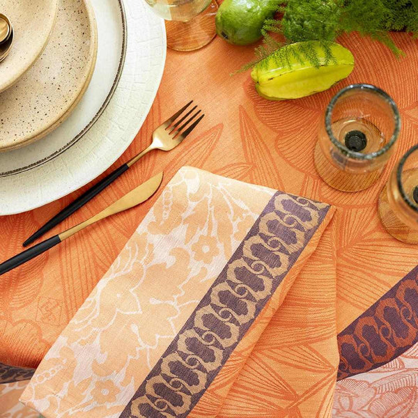 Escapade Tropicale Linen Napkin in Orange by Le Jacquard Français next to gold cutlery.