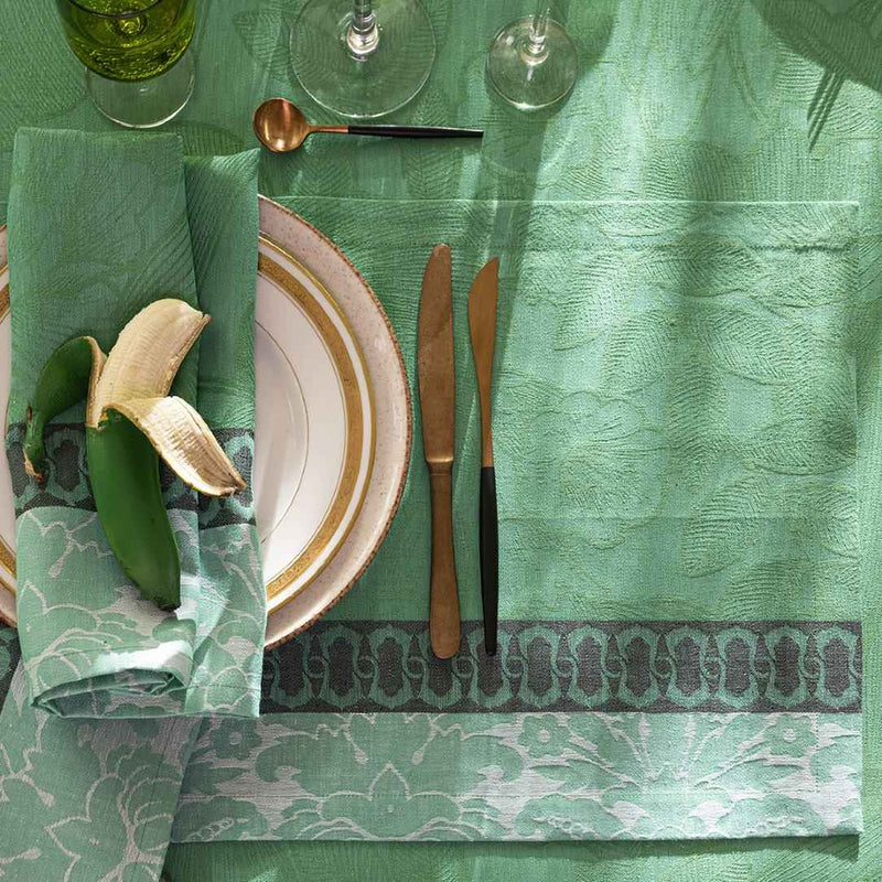 Top view of Escapade Tropicale linen napkin in green by Le Jaquard Francais on tablecloth from the same collection, sold by Amiramour.