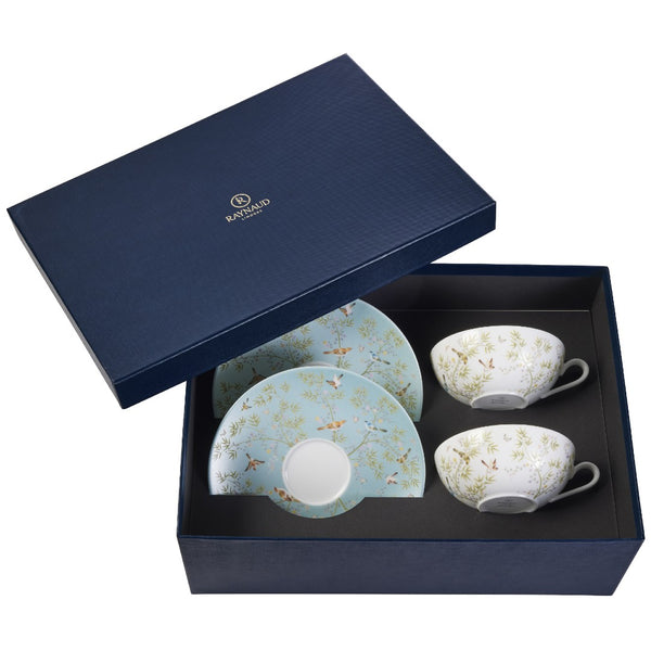 A set of two porcelain tea cups and saucers with turquoise and white color patterns, presented in an open gift box with a navy blue interior lining.