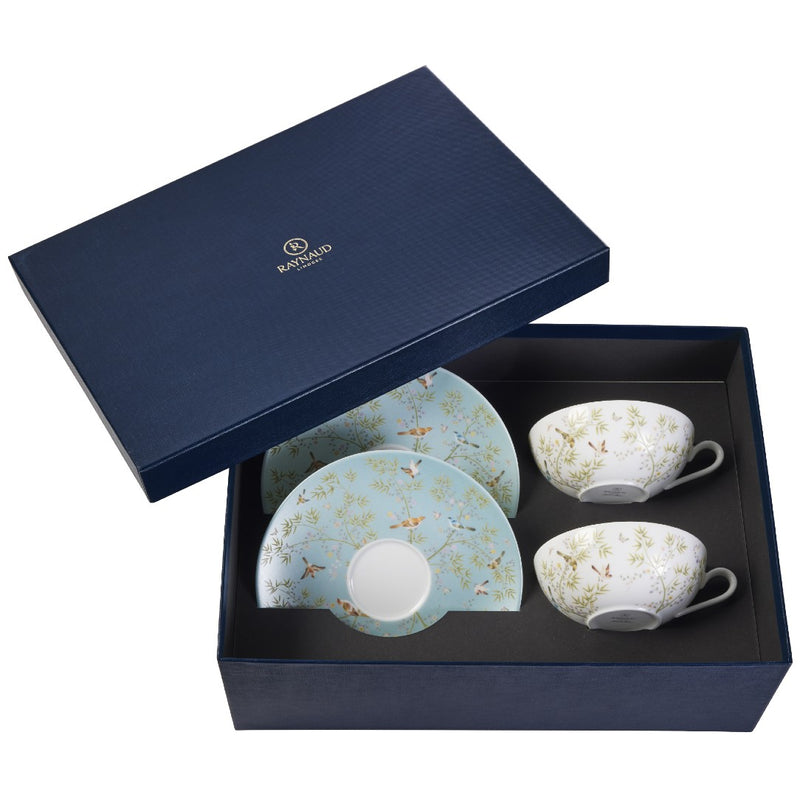 A set of two porcelain tea cups and saucers with turquoise and white color patterns, presented in an open gift box with a navy blue interior lining.