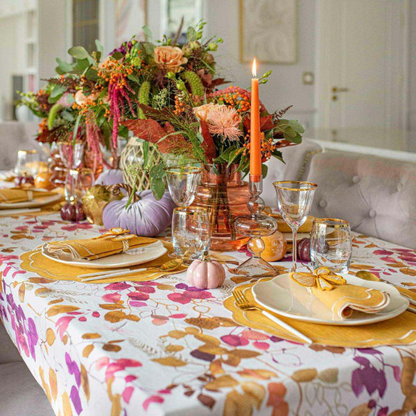 Decorative table setting with floral tablecloth, candles, and pumpkins in a home setting.
