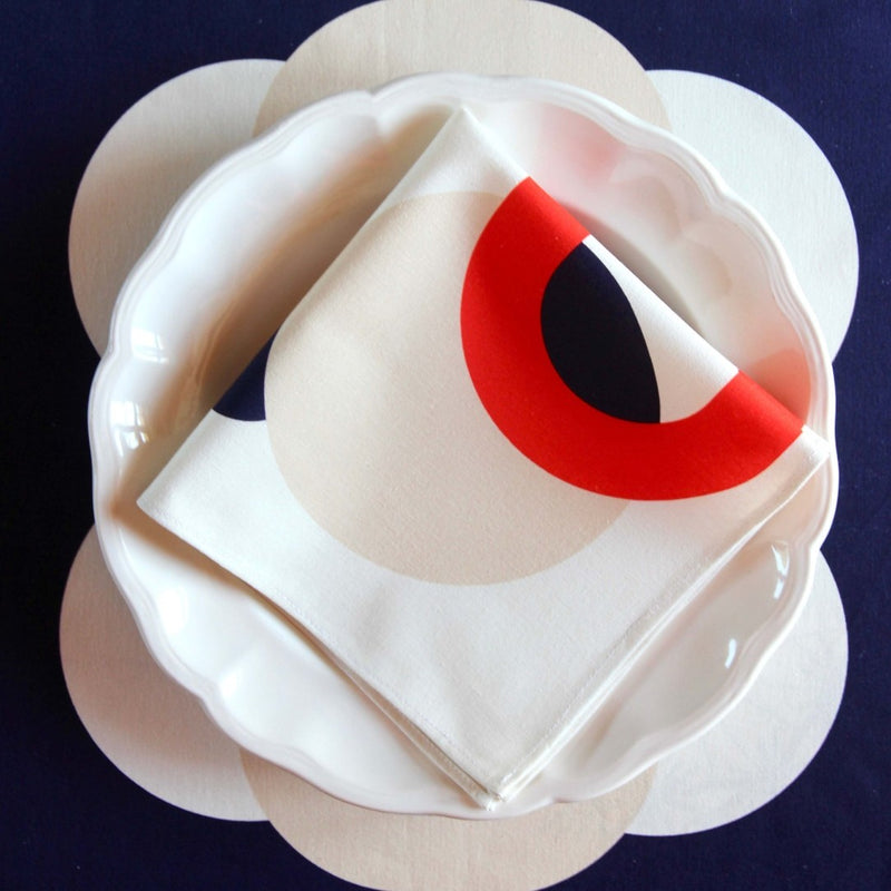 Red, blue, and ivory bubble patterns on Alto Duo ecru luxury napkin fabric, folded on plate.
