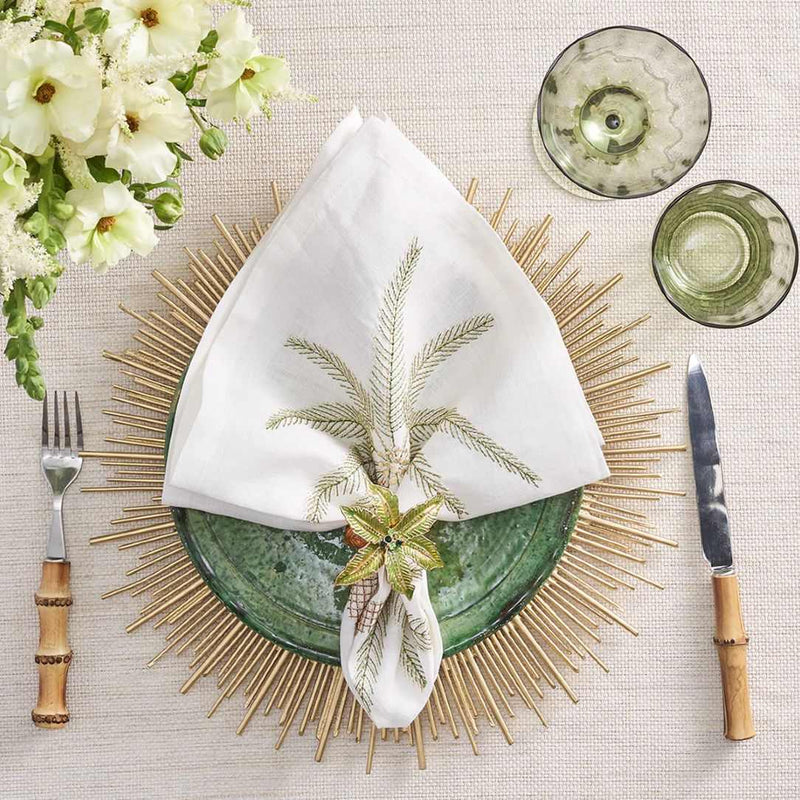 Gold sunburst Radiate charger plate by Kim Seybert styled with white palm tree motif napkin.