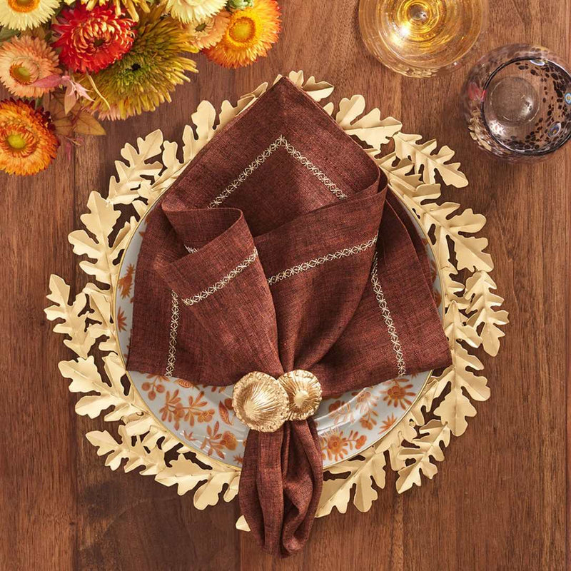 Gold Gilded Leaves charger with layered wreath-like leaf design by Kim Seybert with brown napkin.