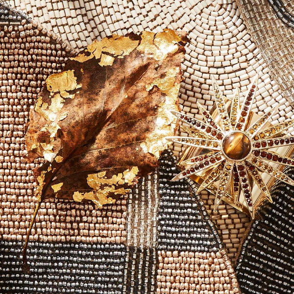 Starburst Napkin Ring placed beside a gold leaf on dark and gold placemats by Joanna Buchanan