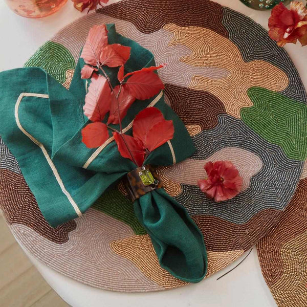 Hunter green linen napkin with gold trim styled in autumn setting with napkin ring on beaded placemat.