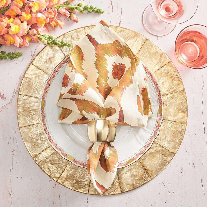 Rust orange Watercolor Ikat napkin by Kim Seybert, styled on table setting with gold placemat and napkin ring.