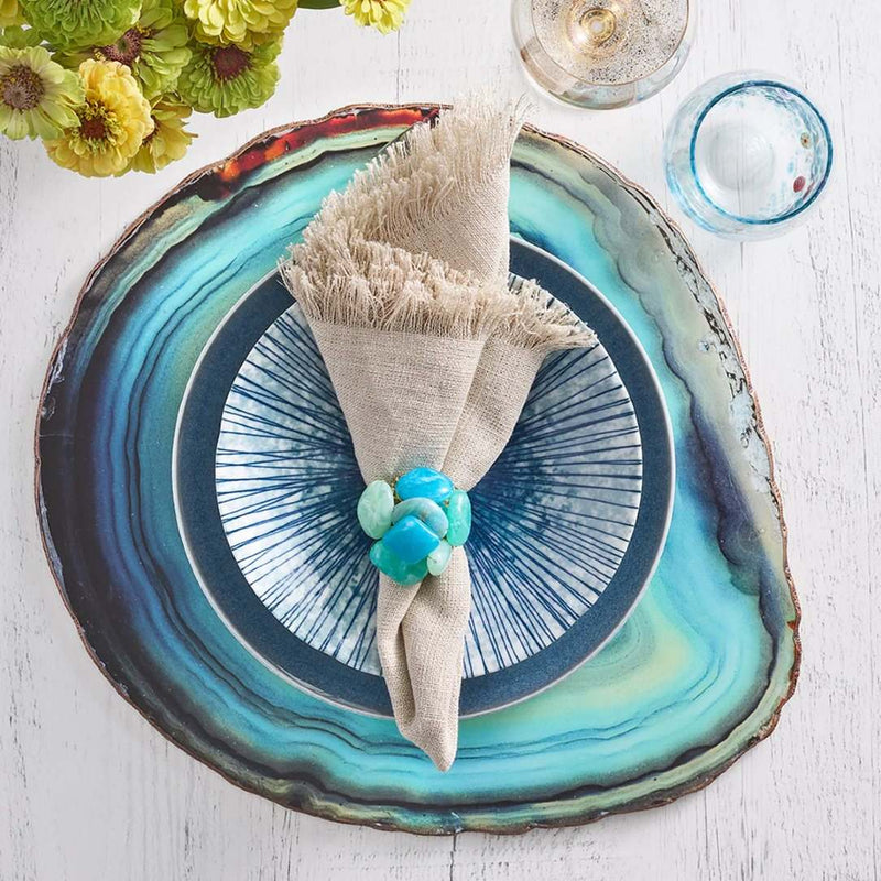 Brown linen napkin with fringe and an organic, textured look by Kim Seybert styled with blue placemat