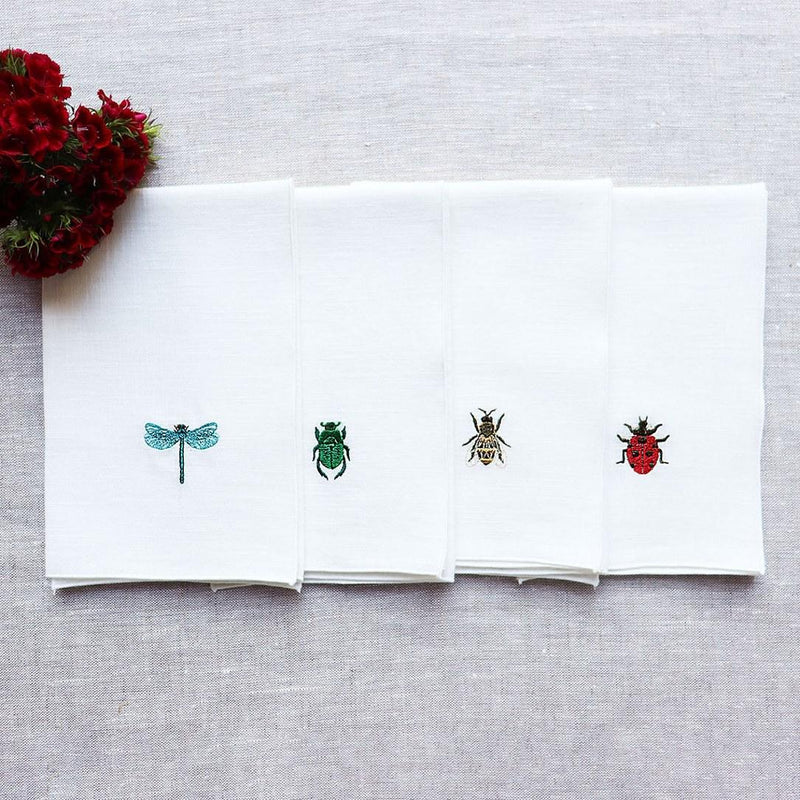Folded Insetti linen napkins embroidered with insect motifs on grey tablecloth