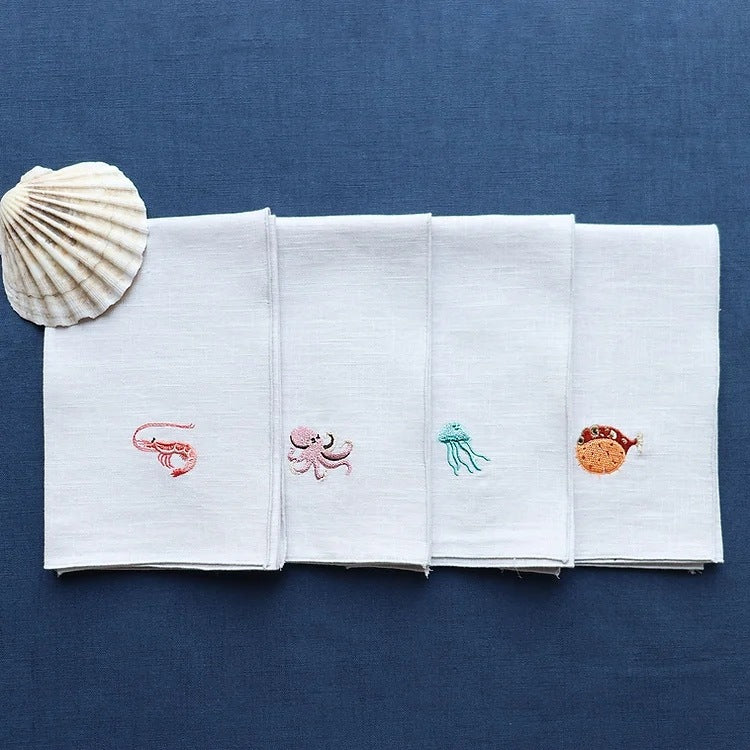 Folded Marina linen napkins embroidered with sea creature on navy tablecloth