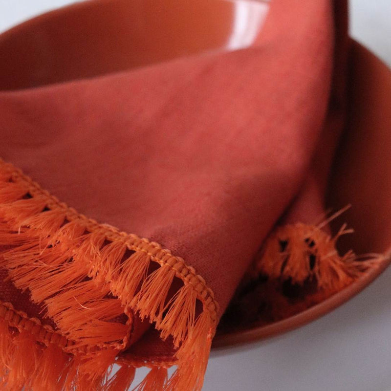 Close-up of the fringe detailing on the orange linen napkin by Giardino Segreto.