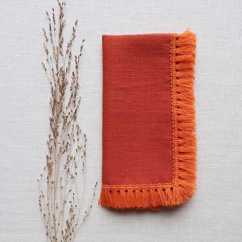 Orange linen napkin with fringe by Giardino Segreto on a white tablecloth, sold at Amiramour.