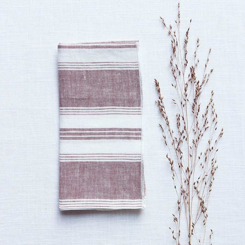 Bordeaux red and white striped linen napkin by Giardino Segreto folded on white tablecloth.