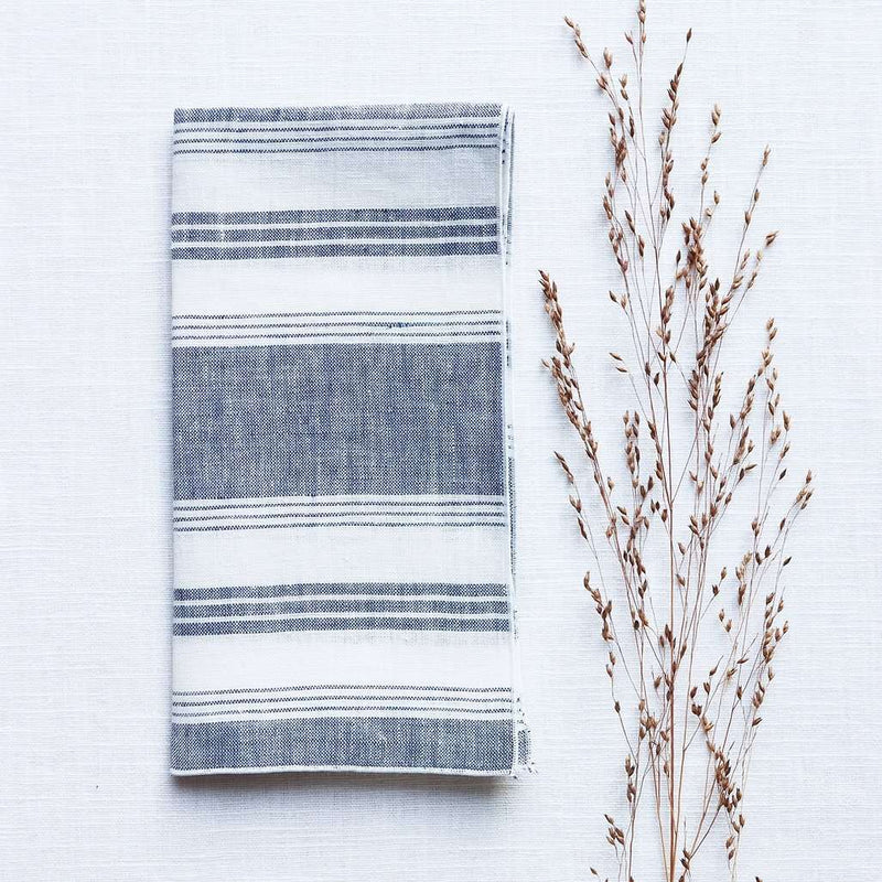 Folded Riva blue and white striped linen napkin with piped edge on white tablecloth 