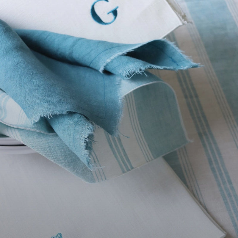 Close-up of the piped edge Riva turquoise and white striped linen napkin by Giardino Segreto