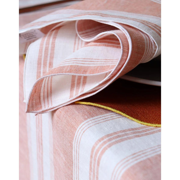 Linen napkin with coral and white irregular stripes close-up on piped border. 