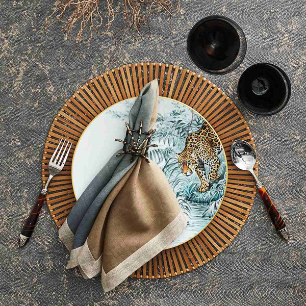 Beige, taupe, and grey linen napkin with metallic foil detail styled on bamboo placemat.
