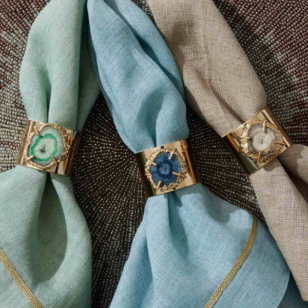 Styled duck egg blue napkin with gold napkin rings on beaded placemat, sold at Amiramour.