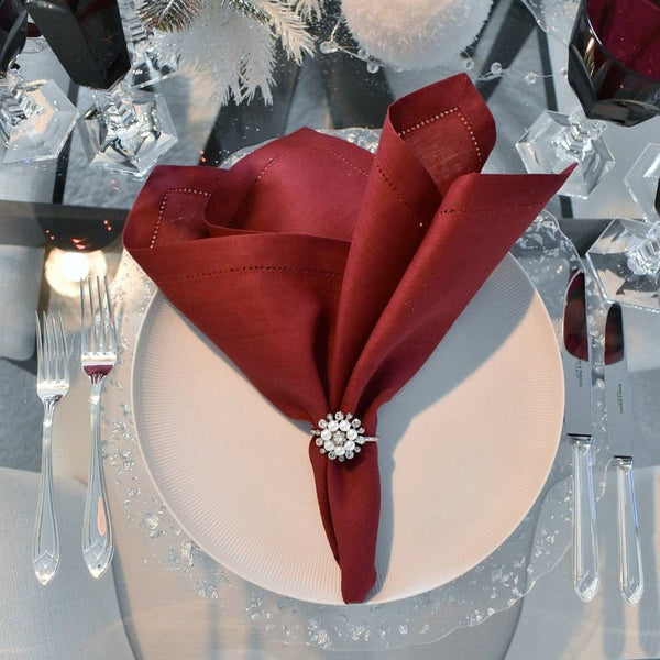 Red napkin folded into a decorative shape with a napkin ring on a white plate, set against a festive background.