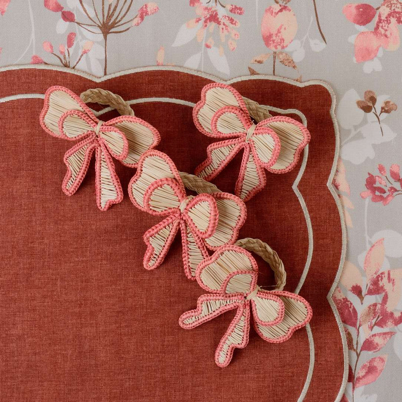 Pink Bows napkin rings by Roseberry Home styled on a brick-red placemat