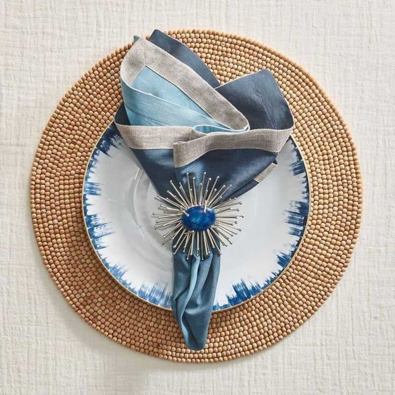 Natural wood bead round placemat by Kim Seybert styled with blue napkin.