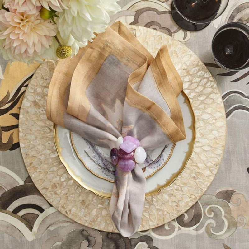 Champagne gold round placemat with hand-cut capiz shells by Kim Seybert styled with purple napkin ring.