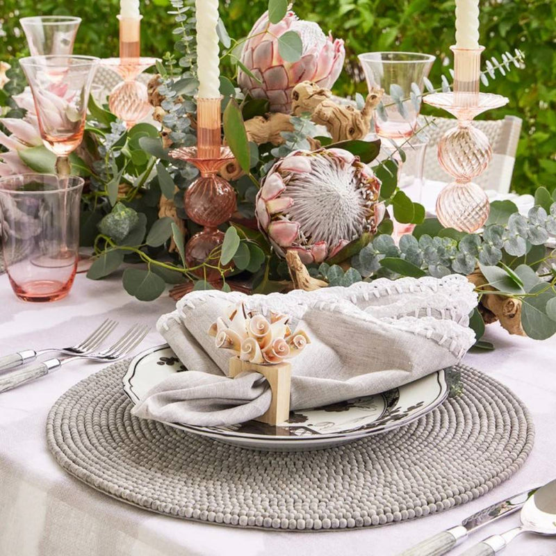 Luxury round placemat in gray with driftwood-inspired beads styled on coastal tablescape.