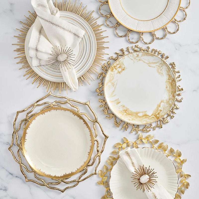 Gold and silver enamel charger with leaf motif by Kim Seybert presented with other plate chargers. 
