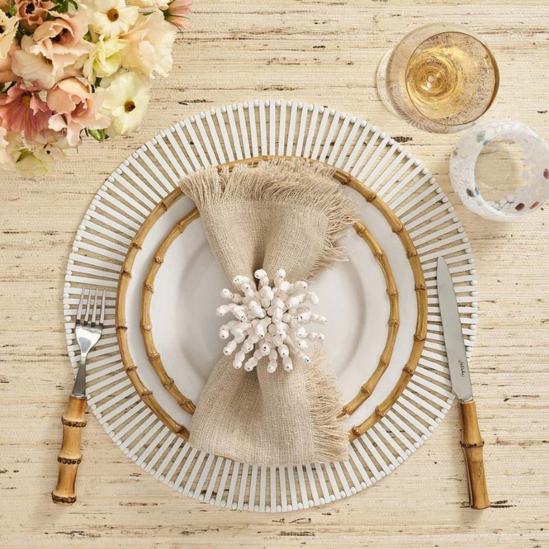 White spoke bamboo placemat by Kim Seybert displayed next to a flower arrangement.