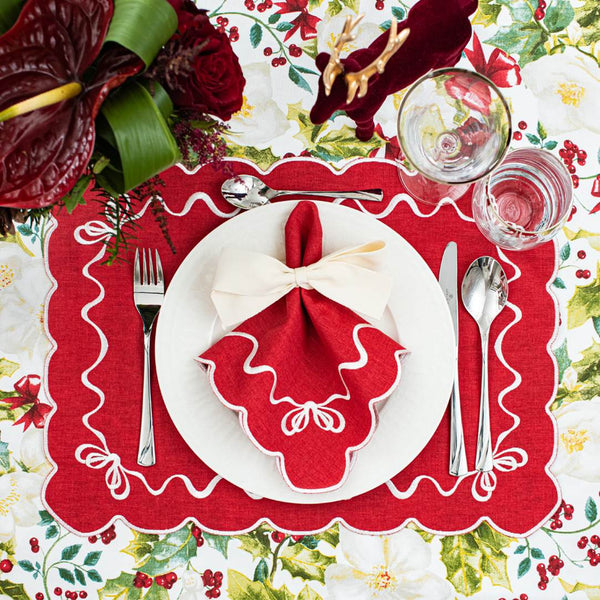 Red cotton placemat embroidered with white Christmas bows styled on traditional tablescape.