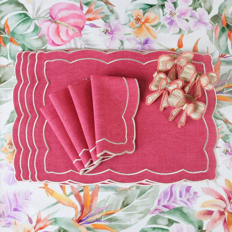Pink placemat with ecru embroidery and irregular wave border with matching napkins on floral tablecloth.