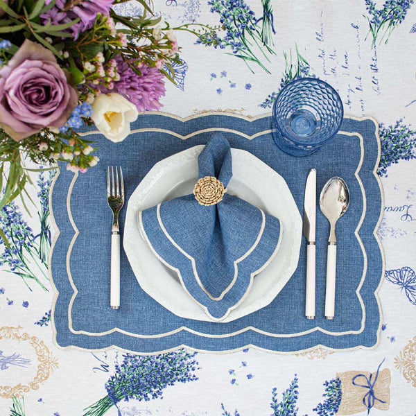 Blue fabric placemat embroidered with ecru thread styled with rattan napkin ring.