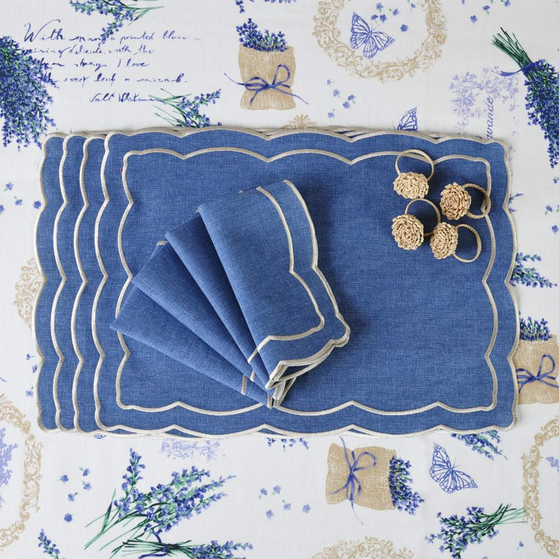Blue fabric placemat embroidered with ecru thread with matching napkins and napkin rings.