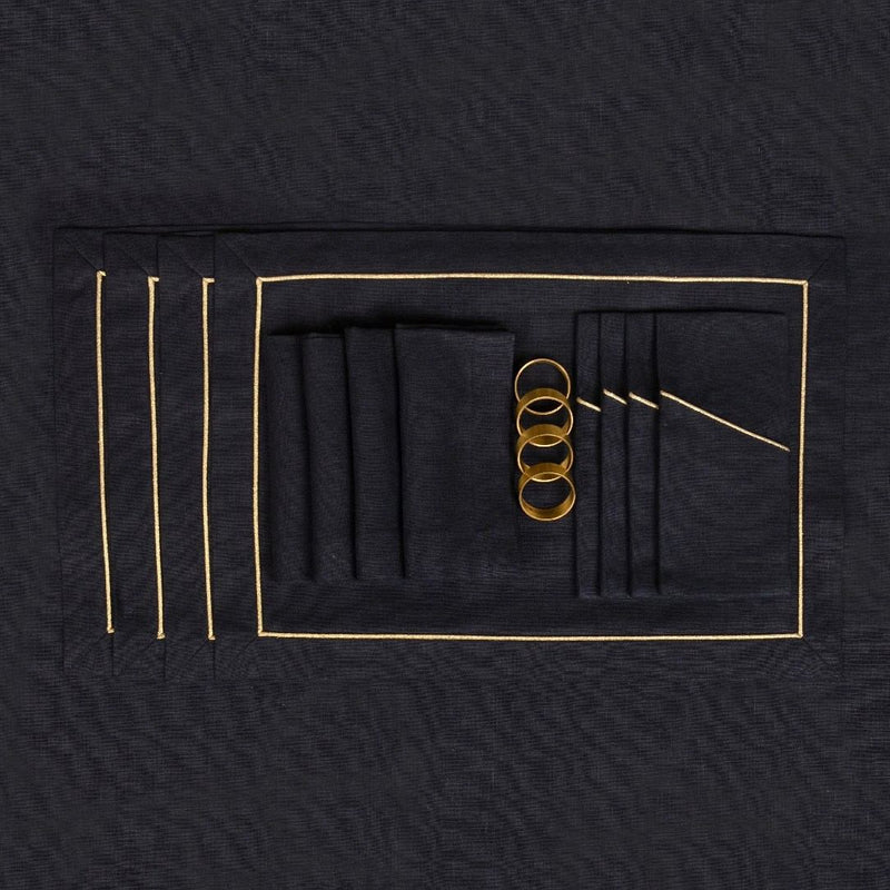 Black linen pocket napkin with gold border presented next to matching tableware.