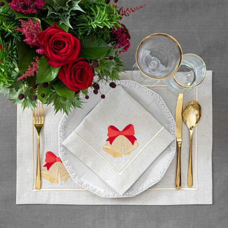 Beige cotton placemat with embroidered Christmas bell and gold border on Christmas table setting.