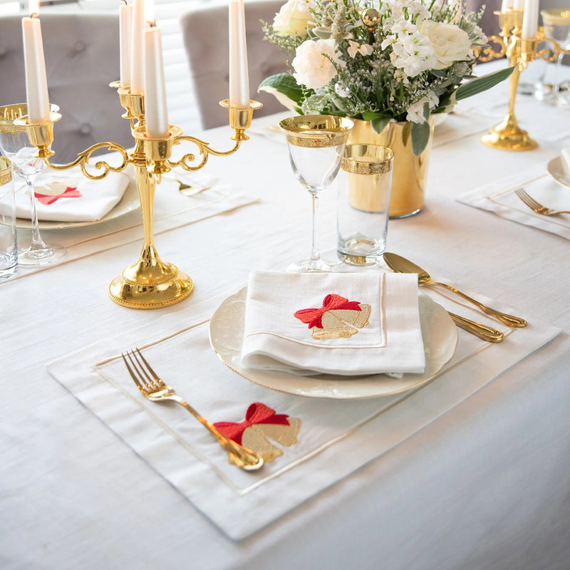 White cotton placemat with embroidered Christmas bell and gold border on festive tablescape.