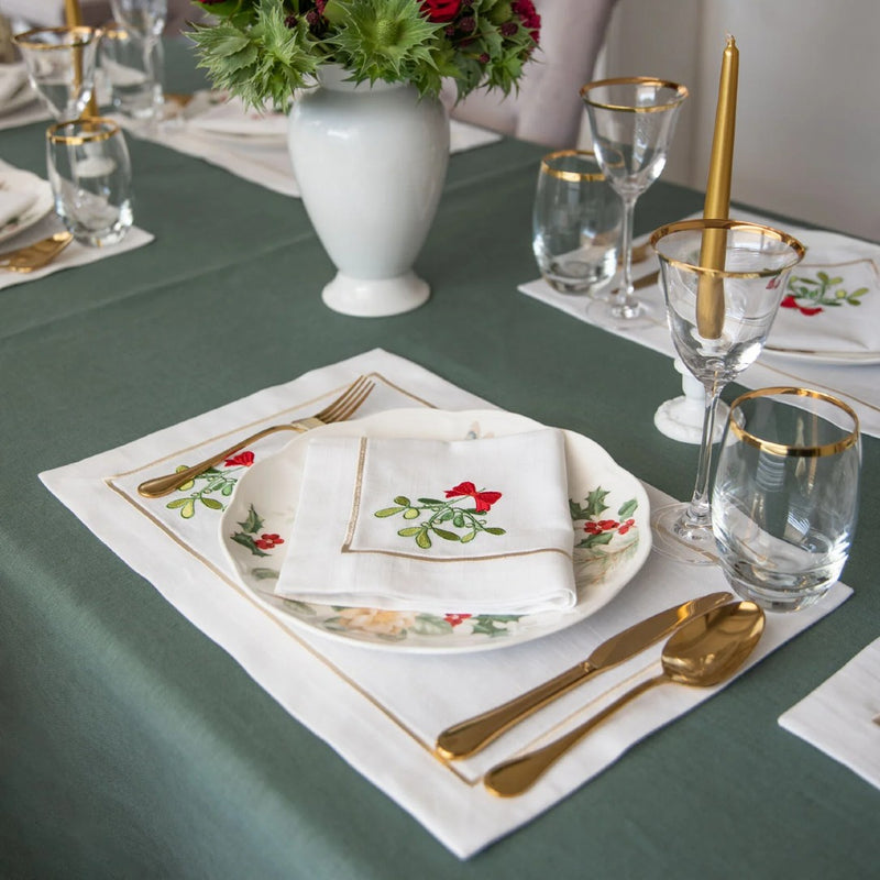 Rectangular white cotton placemat with stitched mistletoe motif on festive table, side view.