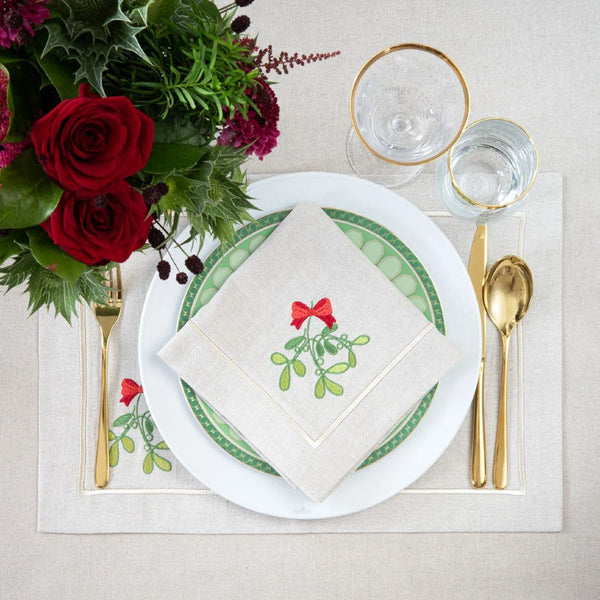 Beige cotton placemat with embroidered mistletoe and gold border on Christmas tablescape.