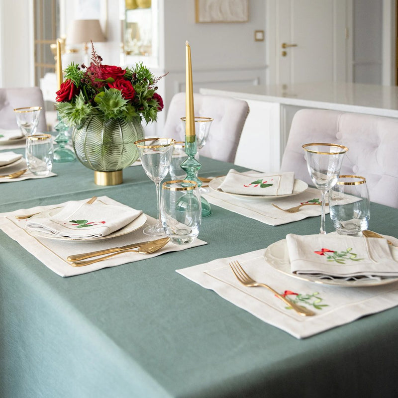 Beige cotton placemat with embroidered mistletoe and gold border on green and gold tablescape.