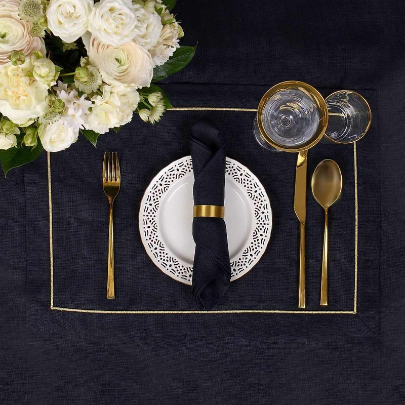 Black linen placemat with gold embroidered border top view styled with gold napkin ring.