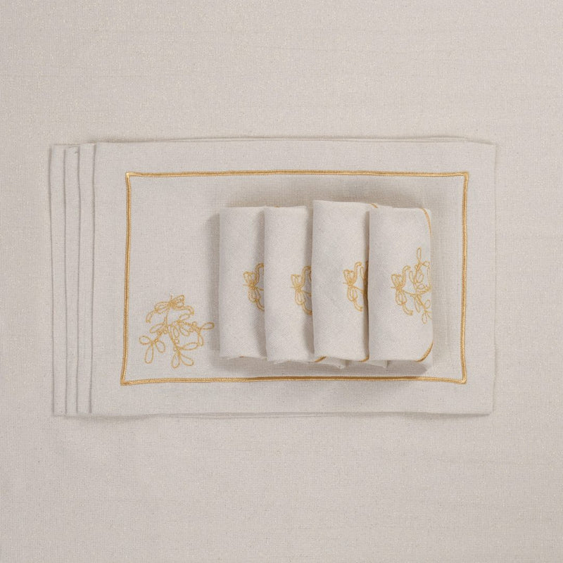 Folded light beige napkins with gold embroidered mistletoe motif on matching tablecloth.