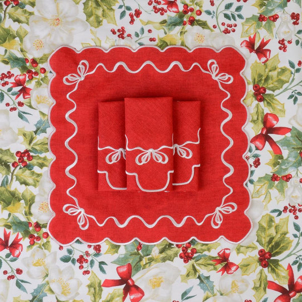 Folded red cotton napkin with white embroidered festive bows in the corners on Christmas tablecloth.